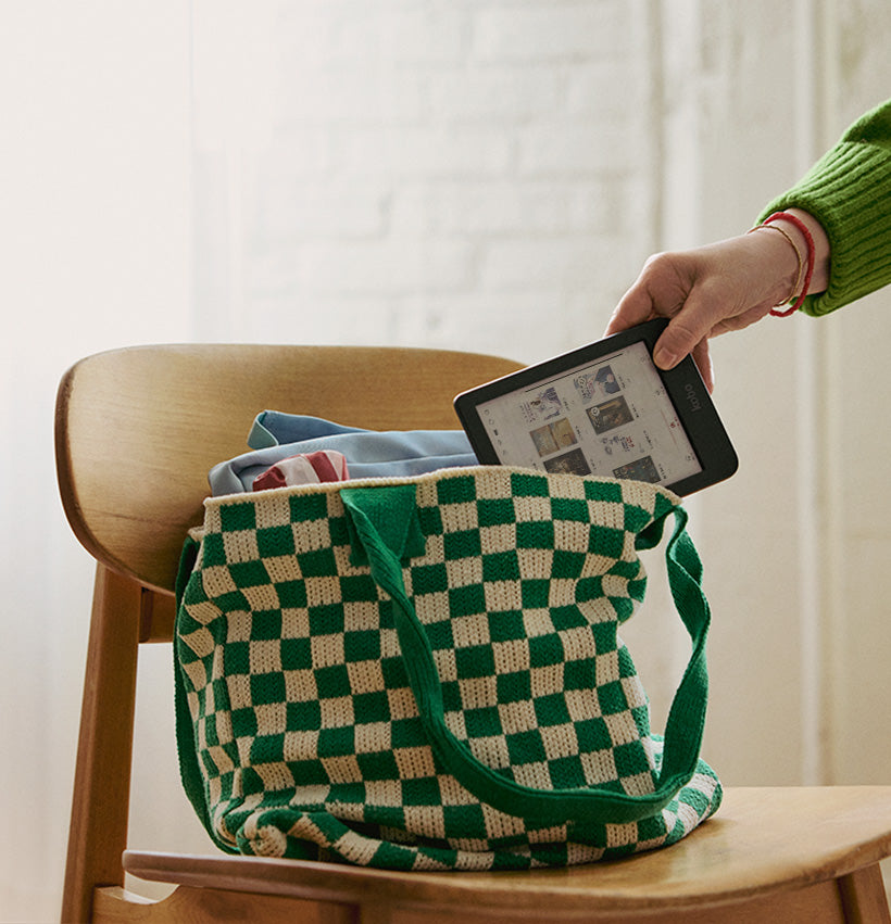 Una mano estrae un eReader Kobo Clara Colour da una borsa posizionata su una sedia di legno.